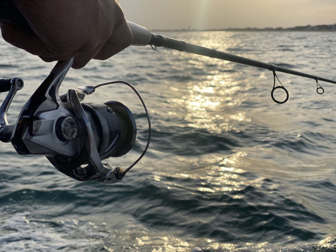 A fishing reel held over the water at sunset